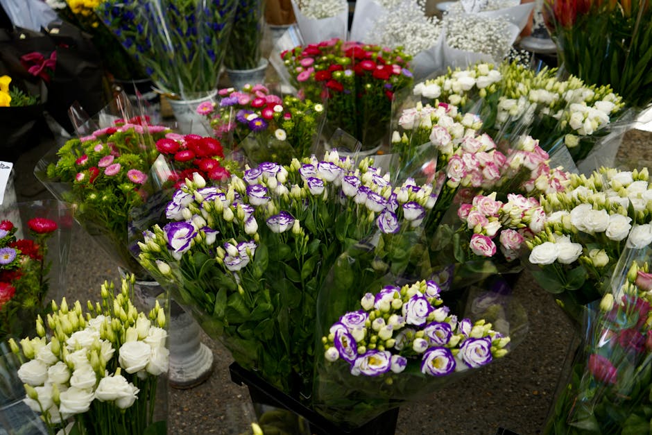 A variety of fresh flower bouquets arranged on a dark surface in a floral shop, featuring an assortment of colorful blooms such as purple and white eustoma, pink and white roses, red carnations, white